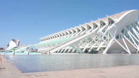 tilt-down view of visitors walking across the frame in front of the science museum within the city of arts and sciences complex in valencia. it is the city's most important tourist destination.