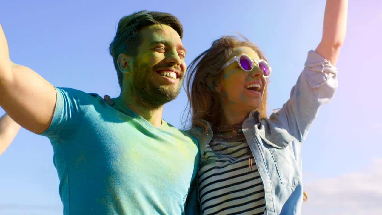 retrato de una pareja feliz cubierta de colorido polvo bailando en el festival de holi. la gente en el fondo se divierten lanzando polvo de holi