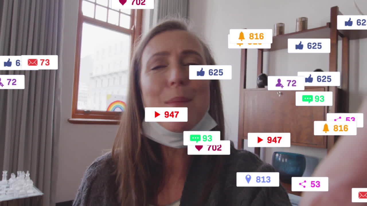 Mature woman creating marketing vlog in home office, interacting with floating social media icons