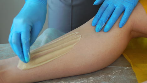 close-up of the hand in rubber gloves is applied to the hair removal paste and by special technology shugaring removes hair