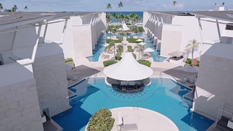 Aerial-forward-over-modern-luxury-pool-area-with-loungers-and-palms,-punta-cana
