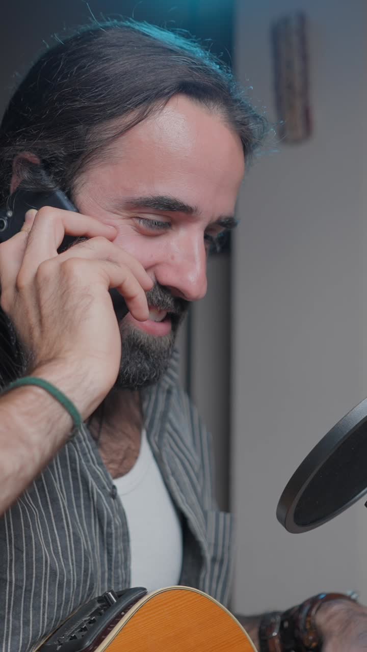 Man on a phone call next to a microphone and guitar