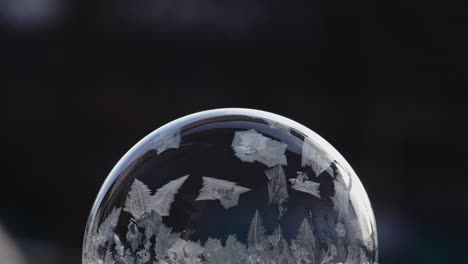 festive background with air balloon ice pattern. a soap bubble lies on the snow on a black background, snowflakes fall on it and freeze