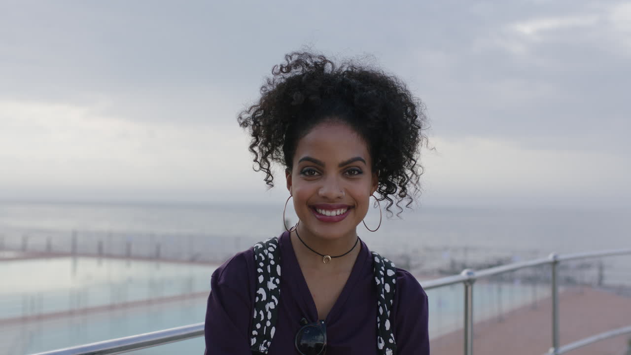 retrato de uma mulher hispânica atraente com cabelos rizados confiante sorrindo alegre pela piscina à beira-mar