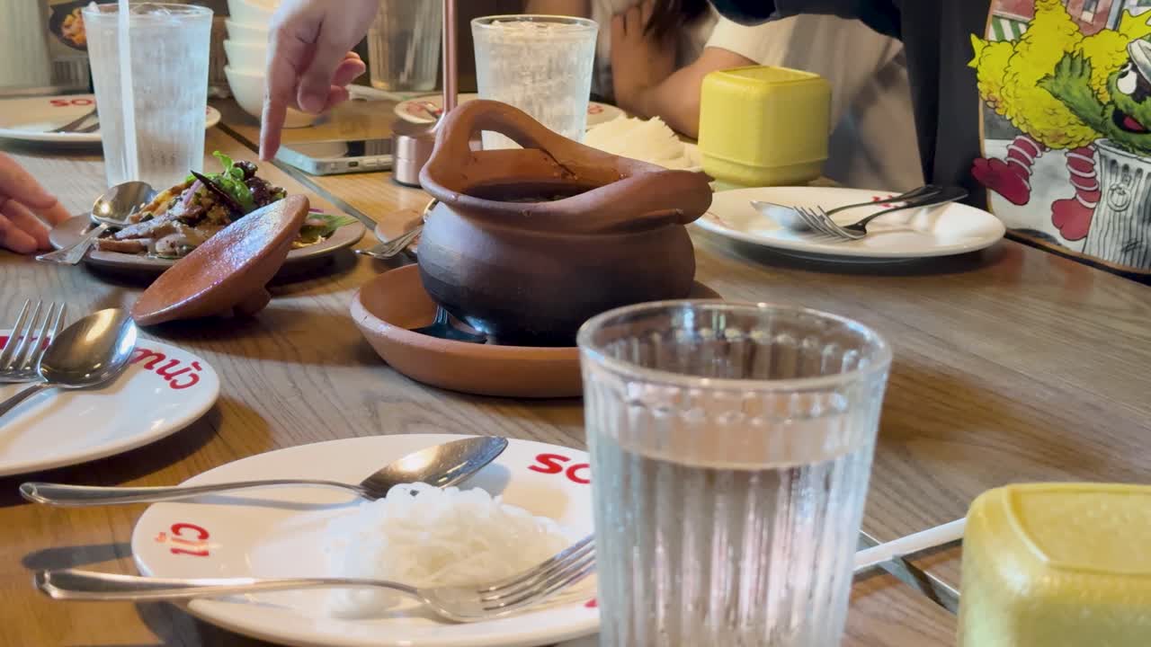 Hænder placerer traditionelle thailandske Isaan retter på et træbord i en lyst oplyst restaurant