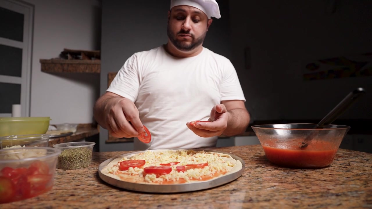 Chef prepara pizza con pomodori appena affettati.