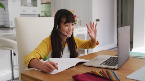 Feliz-Chica-Asiática-En-Casa,-Sentada-En-El-Escritorio-Sonriendo-Durante-La-Lección-Escolar-En-Línea-Usando-Una-Computadora-Portátil