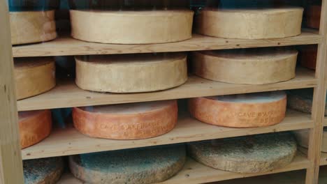 assortment of aging cheese wheels displayed on shelves in small business in france