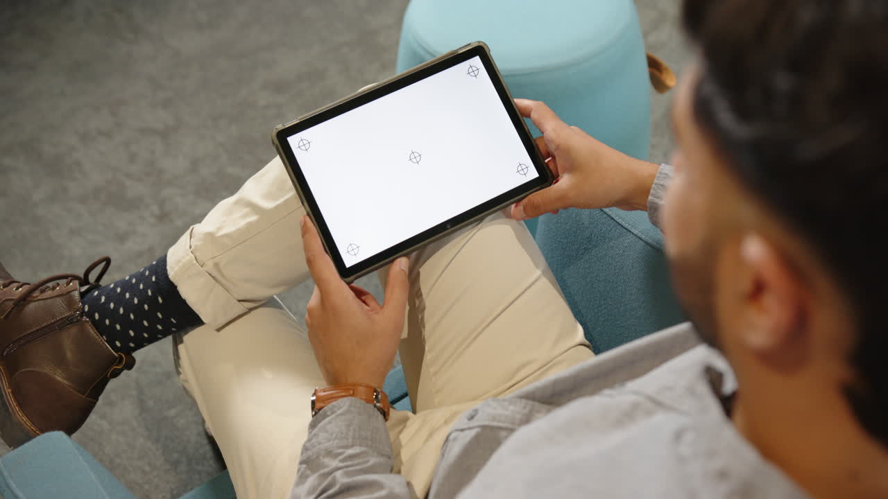 Holding tablet with blank screen, Indian man sitting on couch in business setting