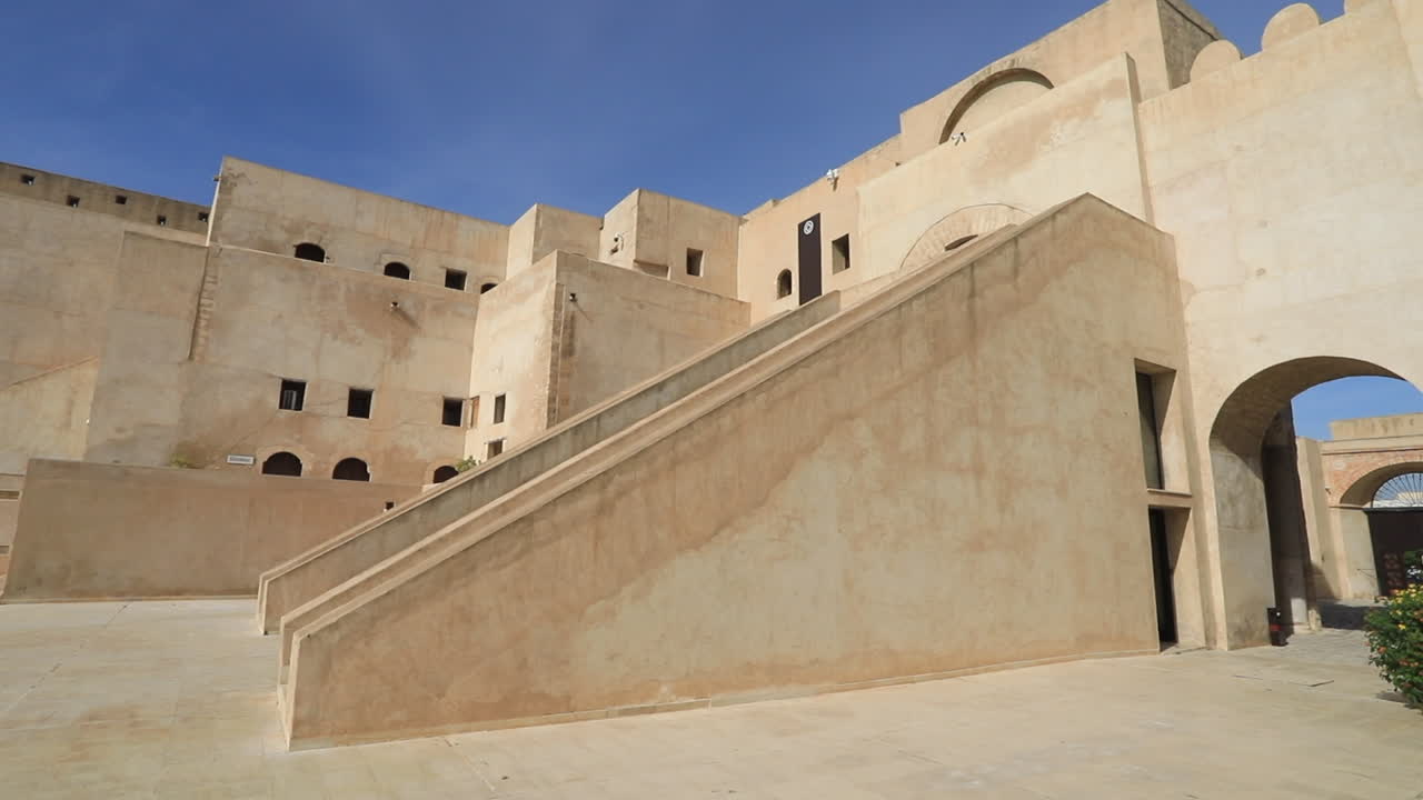 Ancient Tunisian castle with beige stone walls and large archways under a bright blue sky