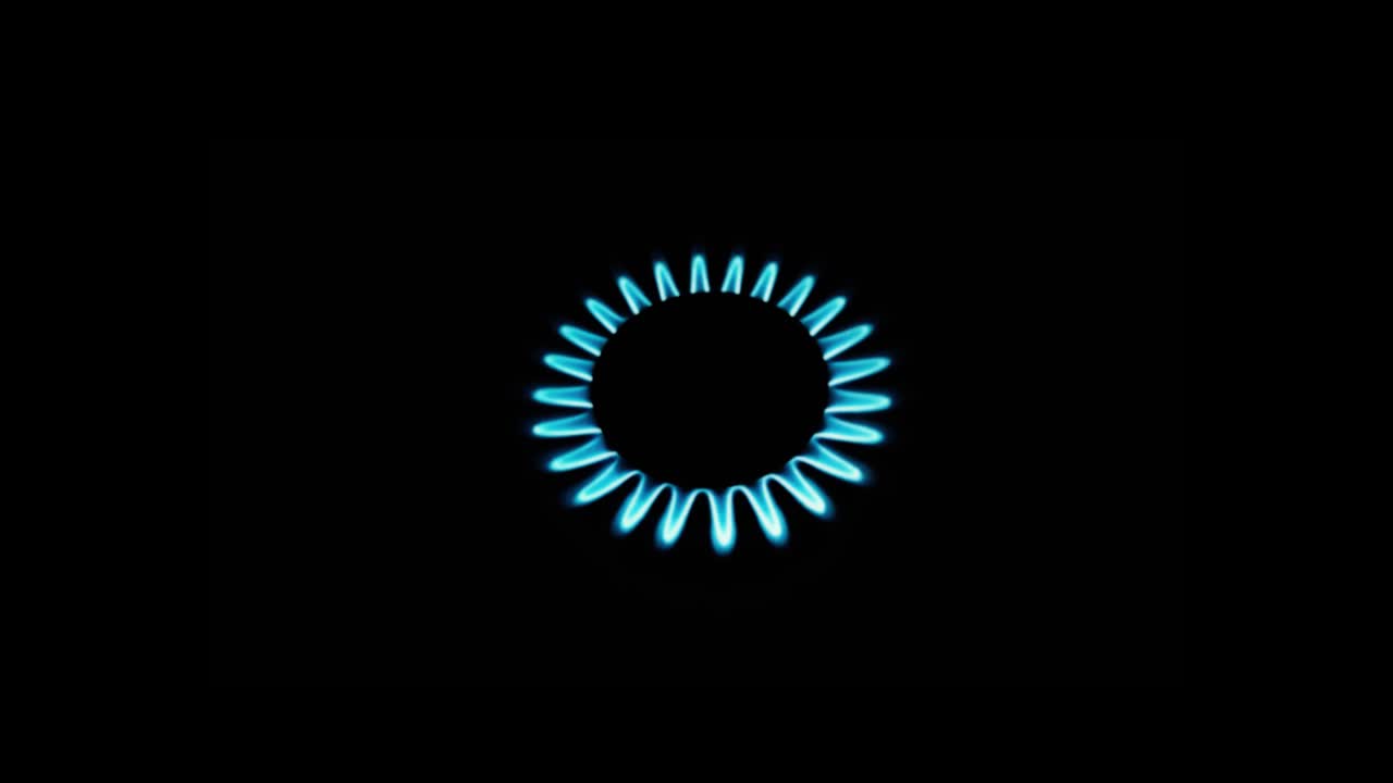 Burning gas stove hob, blue flames macro close-up in the dark on a black background. Gas is switching on, apearing blue flame. Gas stove on isolated on a black background.