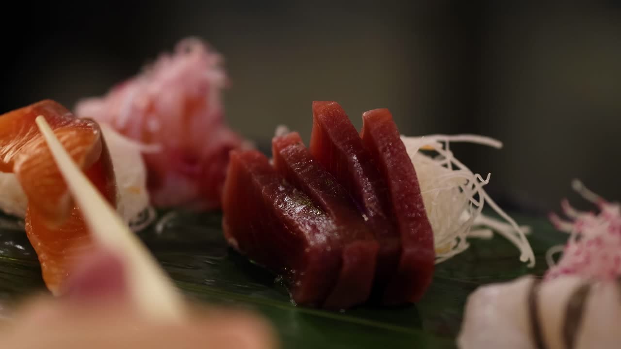 A detailed view of assorted sashimi slices, including tuna and salmon, artfully arranged on a green leaf.
