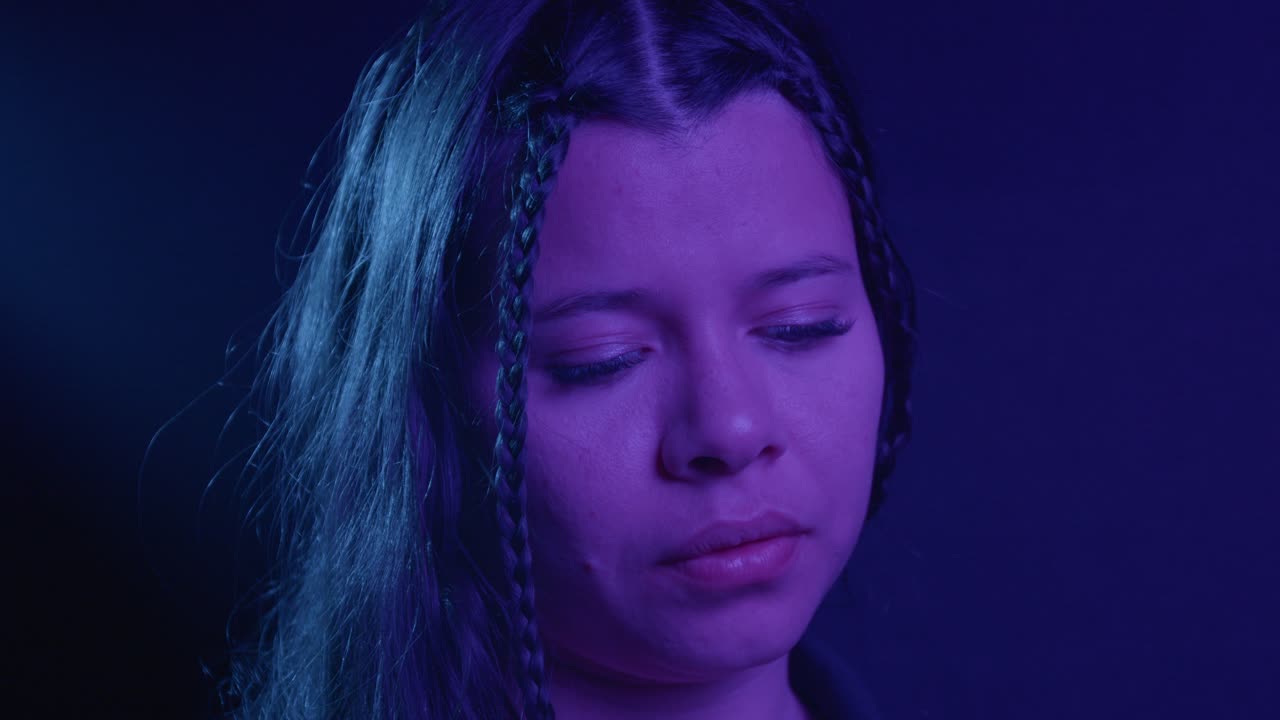 Close-up of a woman's face in a serene, thoughtful moment. Blue and purple lighting creates a soothing, introspective mood. Captured with a detailed focus on emotion and texture