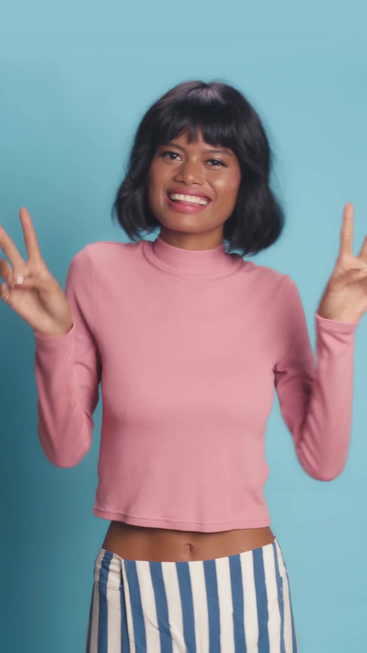 Ragazza in posa con il segno della pace, con top rosa su sfondo blu, allegra.