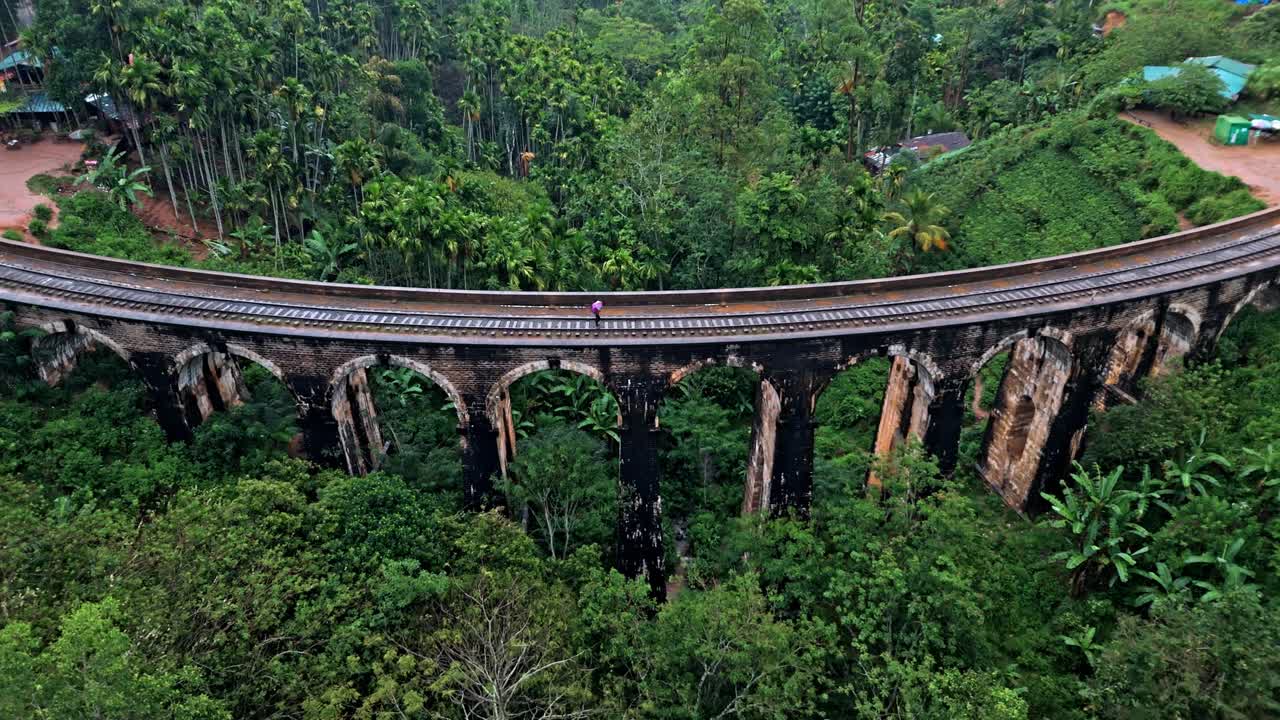 Captivating aerial drone footage of a person crossing the iconic Nine Arches Bridge in Ella, Sri Lanka, holding an umbrella.