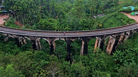 captivating aerial drone footage of a person crossing the iconic nine arches bridge in ella, sri lanka, holding an umbrella.