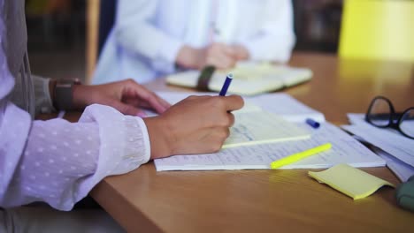 una mujer con las manos escribiendo notas en el bloc de notas. escribiendo ideas de negocios. primer plano de dos mujeres de negocios con las manos escribiendo notas. mujeres irreconocibles con blusas blancas sentadas en la mesa de madera