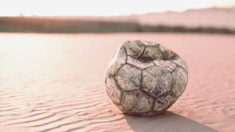 vieja pelota de fútbol desinflada en una playa de arena al atardecer