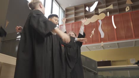 happy multiracial students throwing their mortarboards up in the air. they hug.