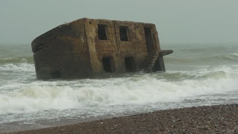 grandes olas tormentosas rompiendo contra las ruinas abandonadas del edificio de la fortificación costera en los fuertes del norte de karosta en liepaja, costa del mar báltico, salpicadura de olas, día lluvioso nublado, plano medio