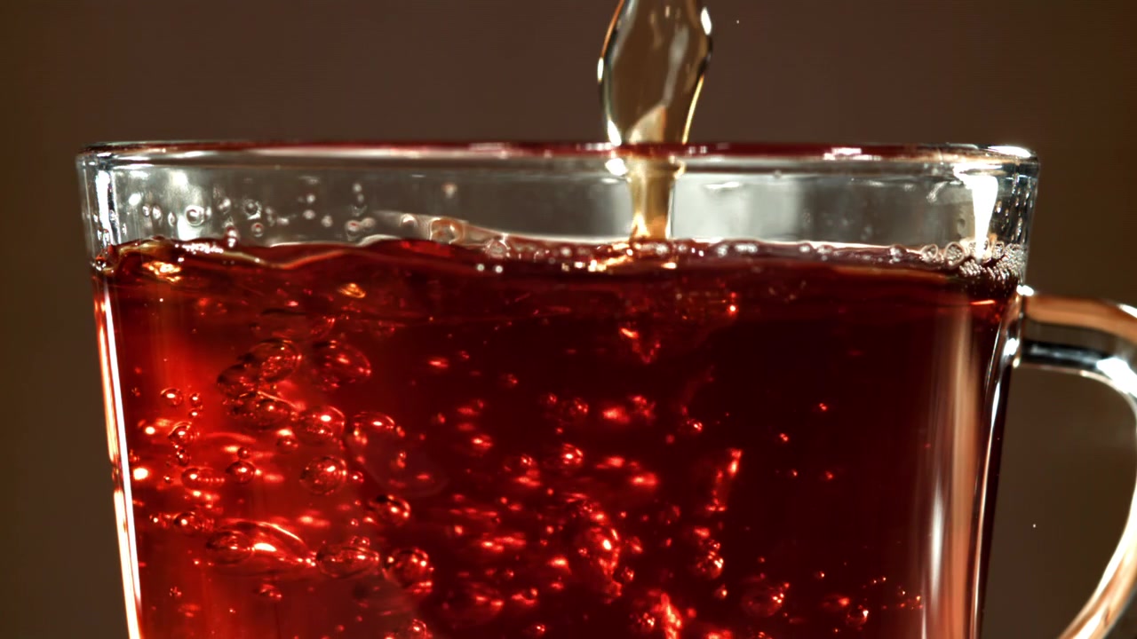 Primo piano di tè rosso scuro versato in una tazza di vetro con bollicine