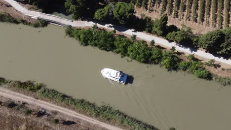 drone looking down on leisure boat on canal with vineyard and cycle path on the bank