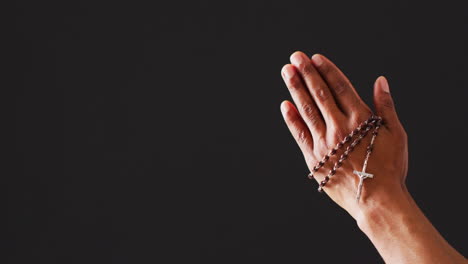 praying hands with rosary on black background with copy space