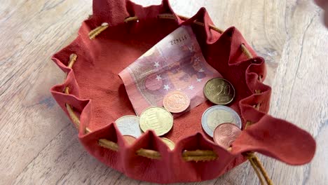 taking euro coins and notes money out of an old fashioned leather purse with draw strings