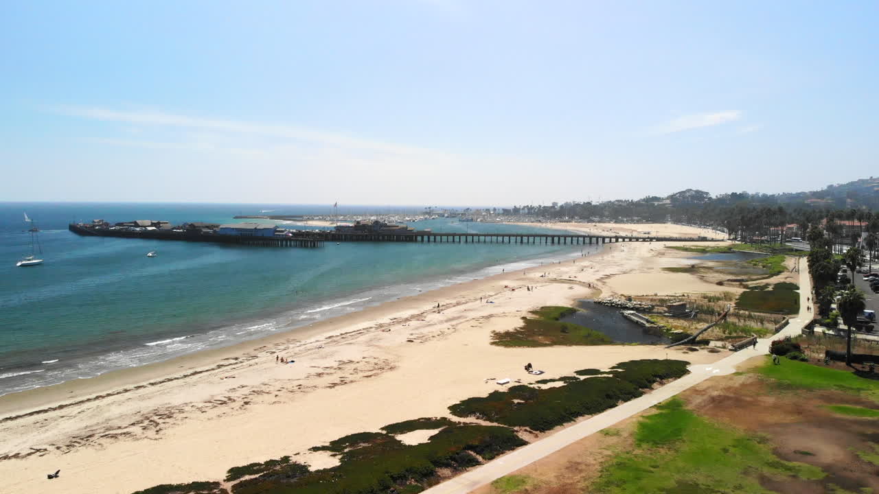 캘리포니아주 산타바바라에 있는 햇살 가득한 해변의 날 스턴의 부두 부두 옆에 있는 짙은 푸른 태평양 항구에 있는 돛배를 바라보는 항공 샷