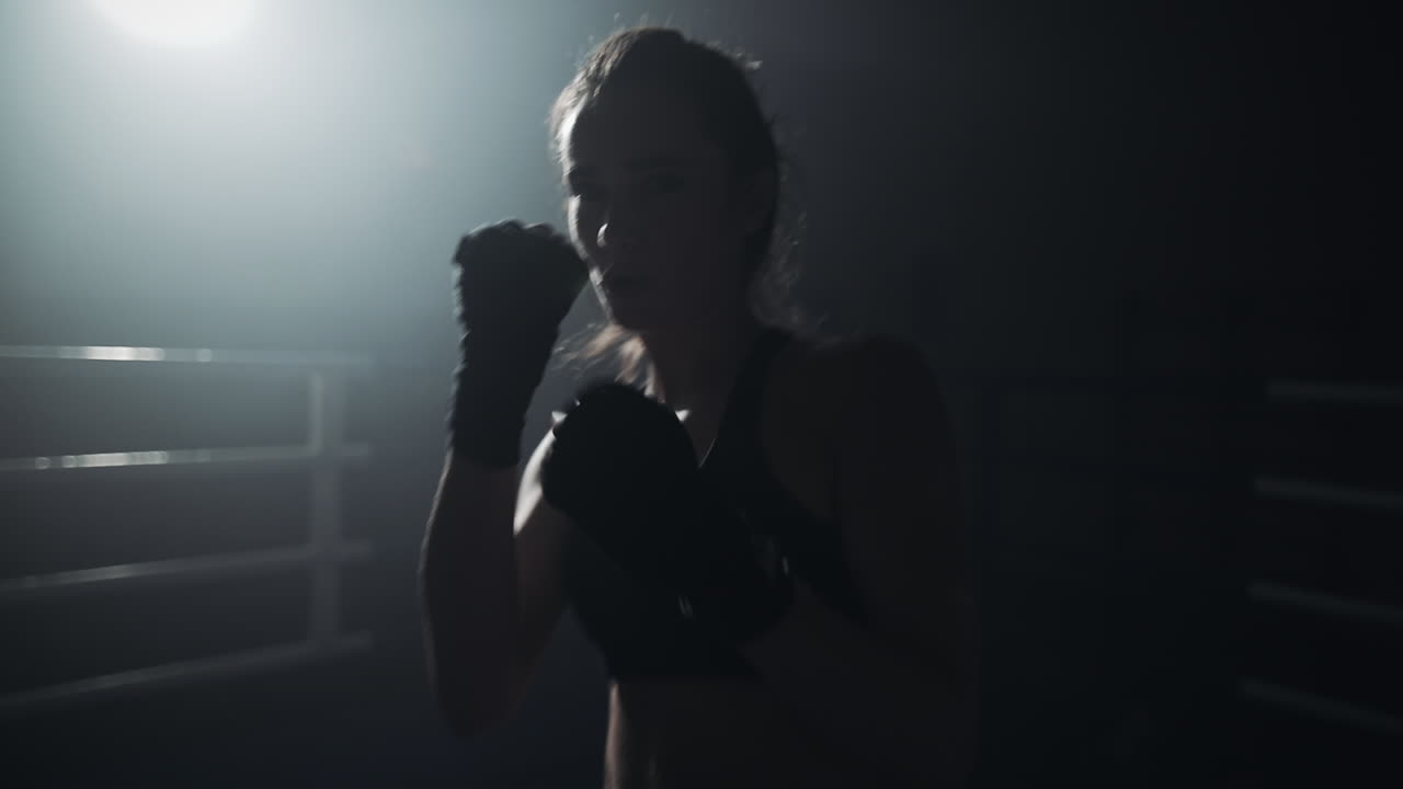 Donna che si allena sul ring di pugilato con illuminazione drammatica
