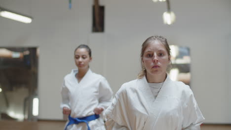 vista frontal de chicas enfocadas realizando posturas de karate en el gimnasio