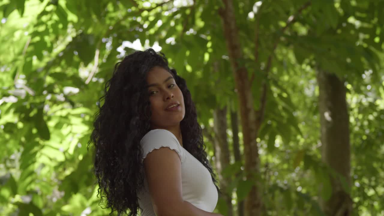 Jolie mannequin latine jouant avec ses cheveux, plan en contre-plongée dans un parc