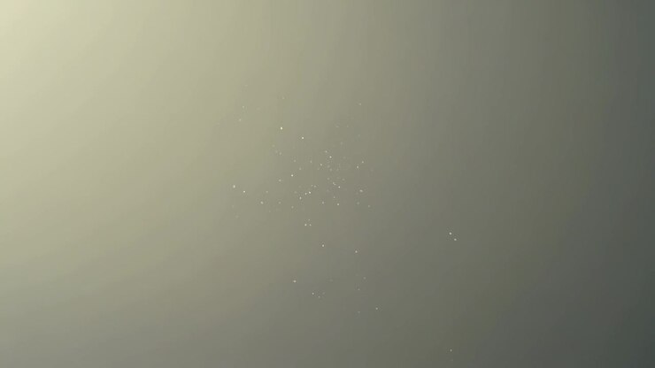 Drifting bright speck cluster changing shape as frames advance on neutral backdrop lit upper-left