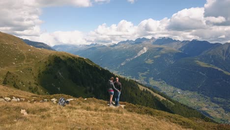 Tiro-De-Dron-Girando-Detrás-De-Una-Pareja-De-Hombres-Y-Mujeres-De-Pie-En-Una-Montaña-Con-Vistas-A-Un-Valle-En-Suiza-En-4k