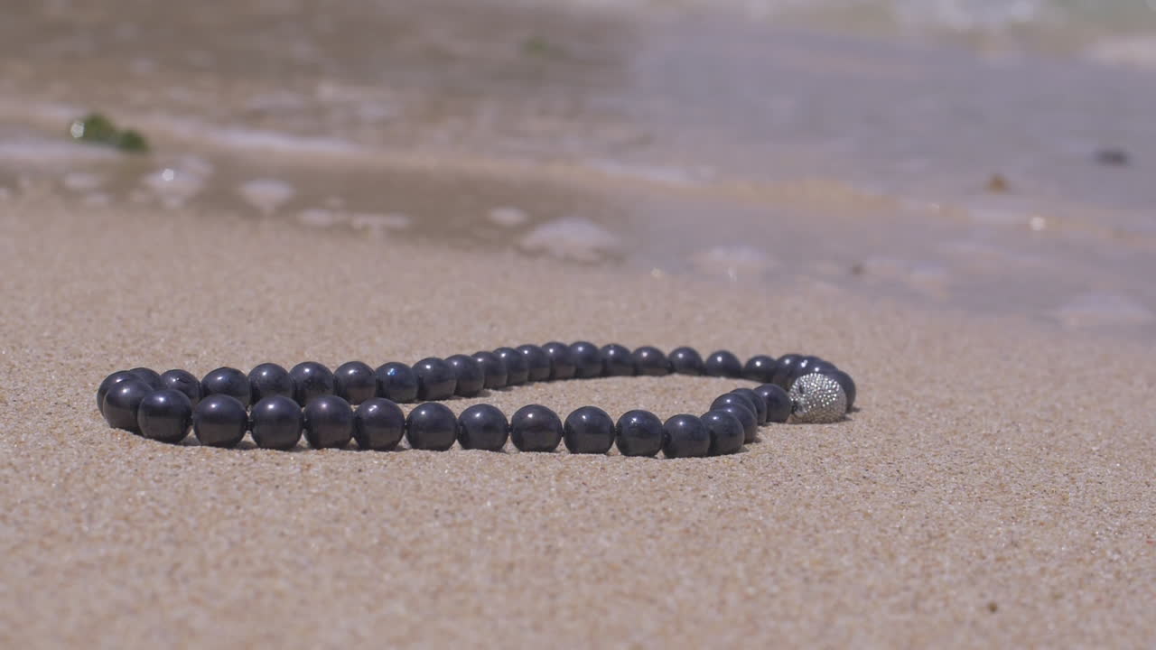 Ripresa cinematografica di una collana di perle con gioielli d'argento adagiata su una spiaggia di sabbia vicino all'oceano, 120 FPS, Slomo