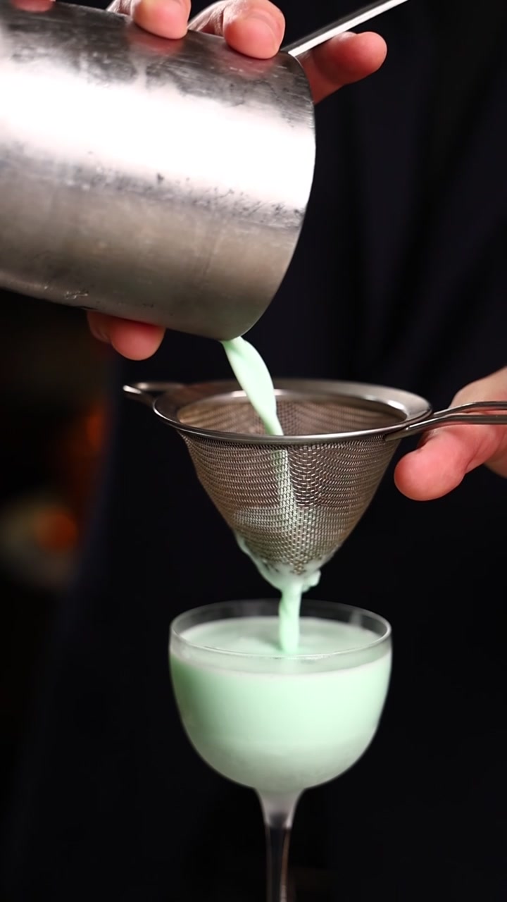 Barman che filtra un cocktail cremoso alla menta in un bicchiere