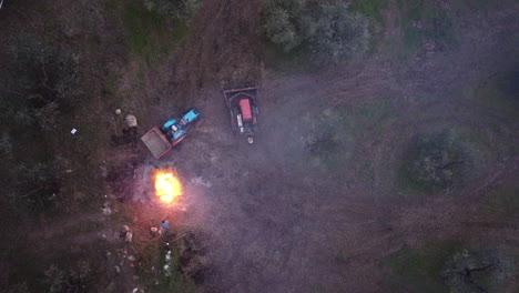 farmer near his tractors working on the narrow rows of green vineyards burning agriculture waste plants