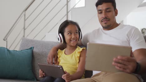 Feliz-Padre-E-Hija-Hispanos-Sentados-En-El-Sofá-Usando-Tabletas