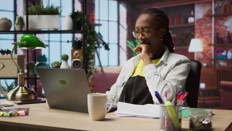 woman in home office stretches back, feeling fatigued while working on laptop