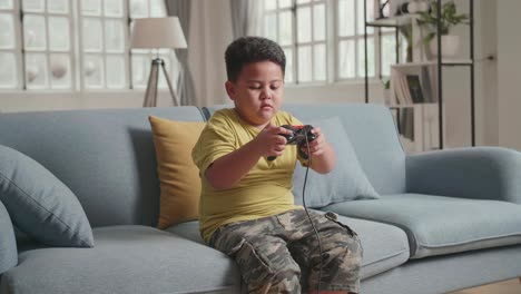 serious boy playing computer game with joystick in living room, feeling unhappy with his loosing game