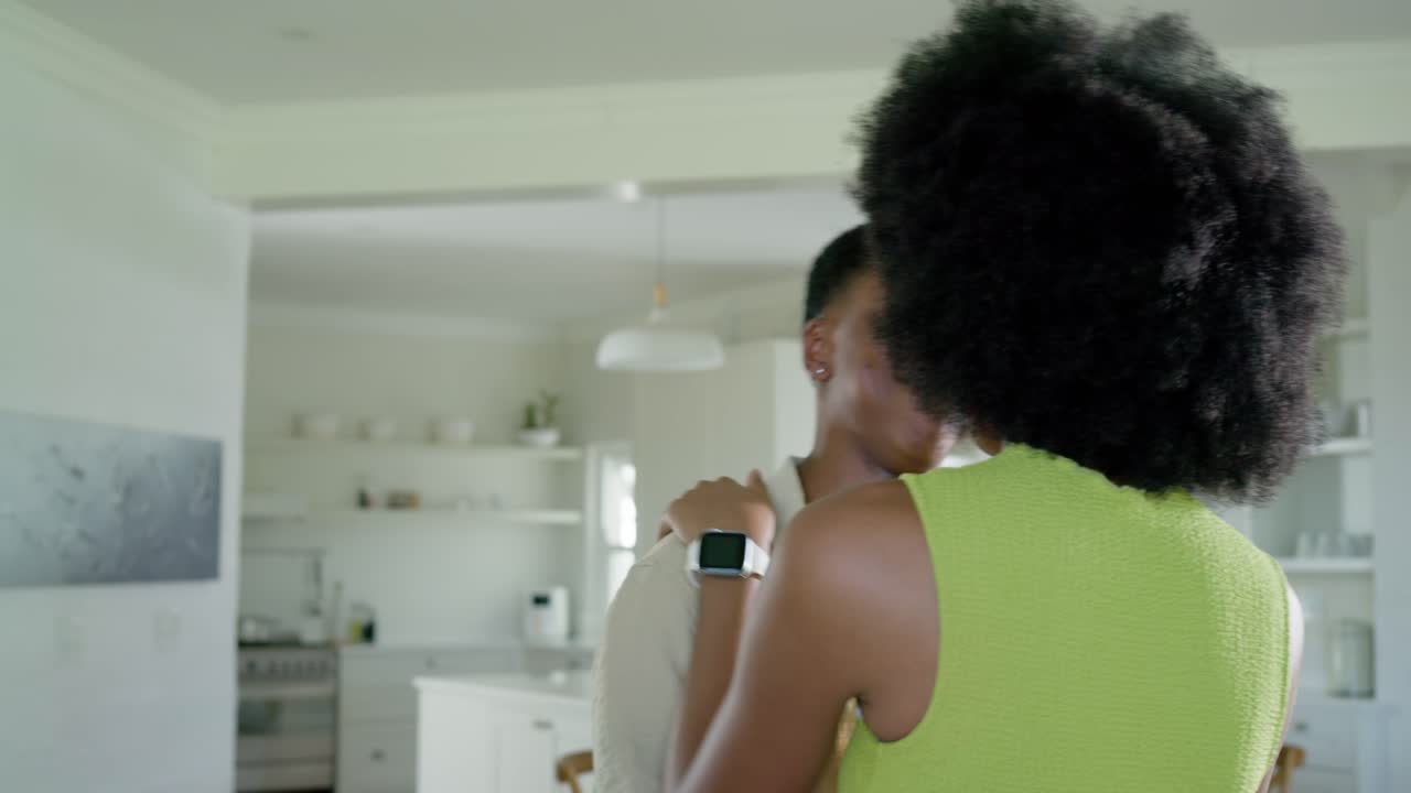 Coppia afroamericana che si abbraccia e si coccola in una cucina luminosa vicino all'isola con smartwatch visibile