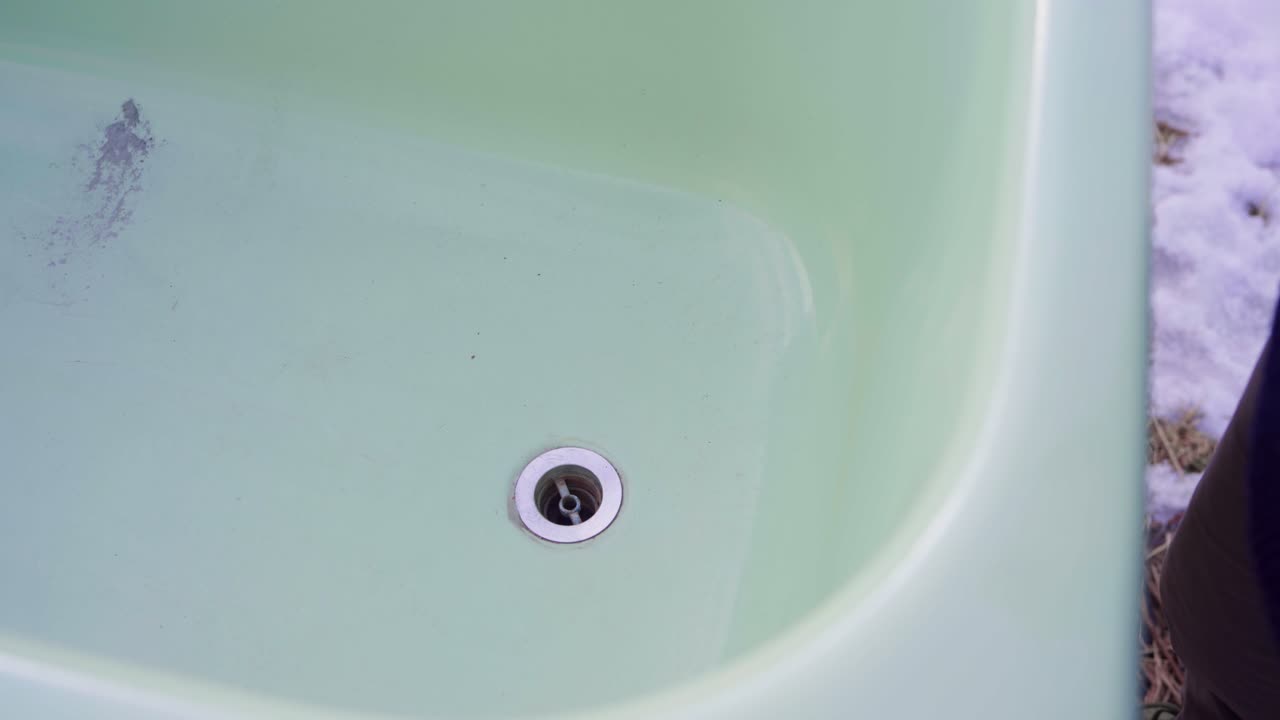 한 남자가 뜨거운 욕조에 배수막을 입하고 있다.