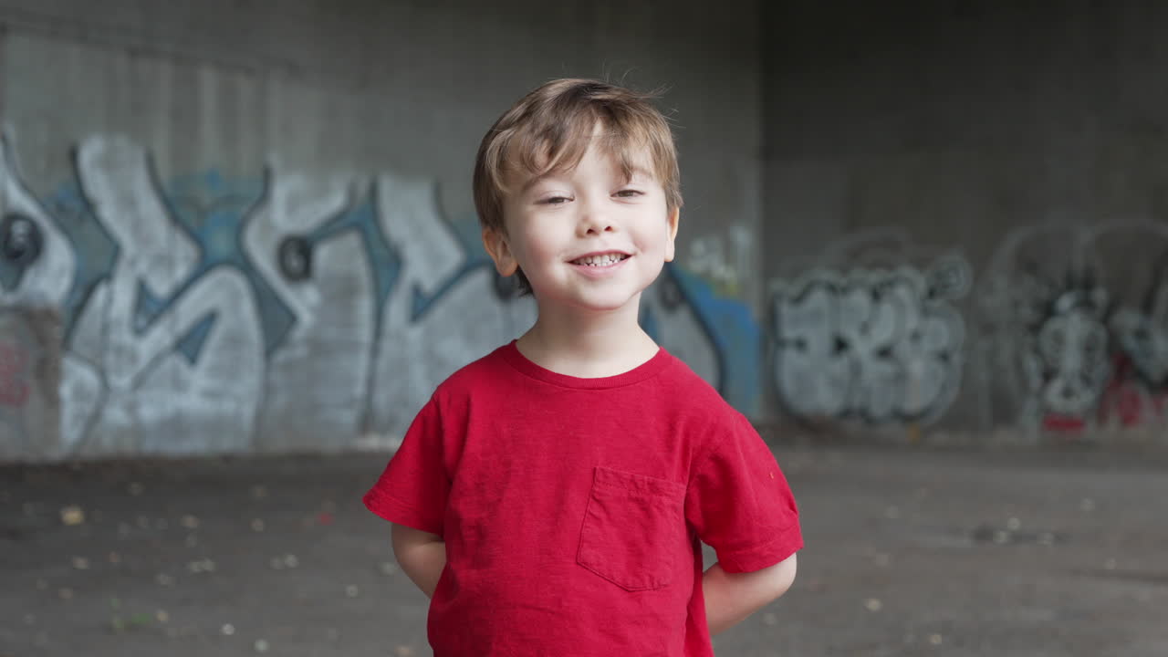 un niño pequeño se está divirtiendo y haciendo expresiones graciosas frente a la cámara con una camiseta roja