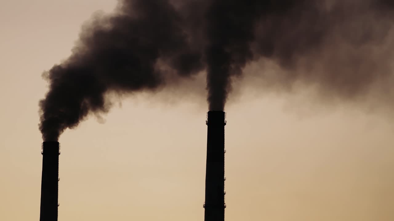 Black dense smoke comes from industrial pipes. Chemical smoke pollute the atmosphere of the evening sky. Close-up.