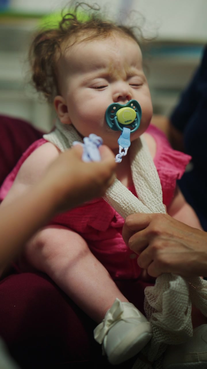 Close up of an infant resting in a supported position while the mother places a pacifier in the baby's mouth during a pediatric mobility and developmental therapy session