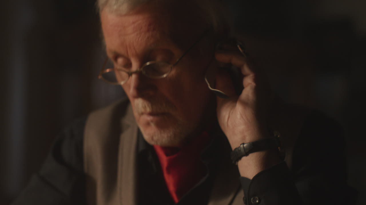 Older passionate man evaluates an old watch in his office at night