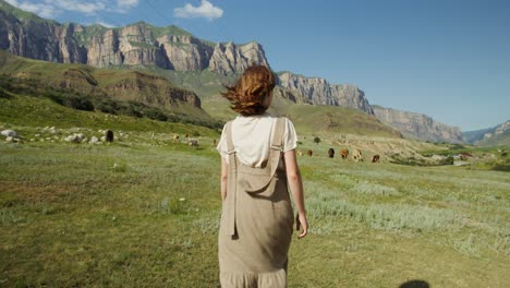 woman walking through a mountain valley with cows