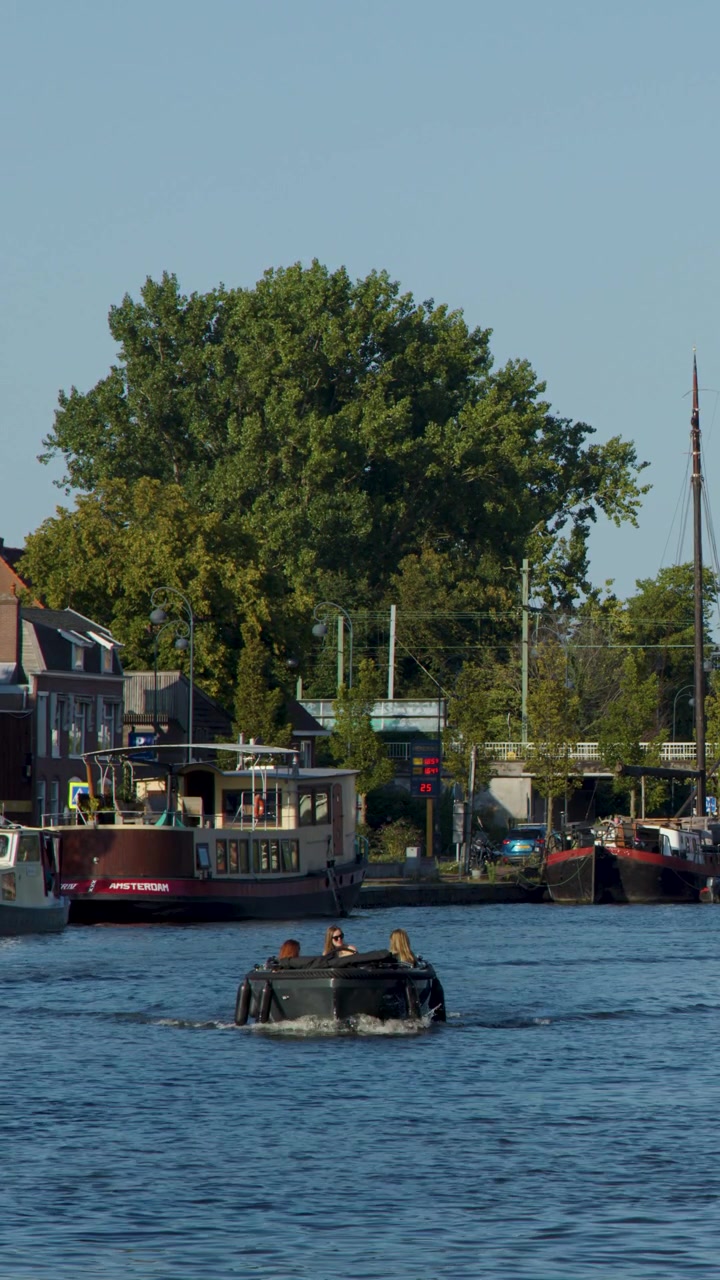 Tre persone a bordo di un piccolo motoscafo viaggiano verso la telecamera su un canale soleggiato di Amsterdam, inquadratura stabile.