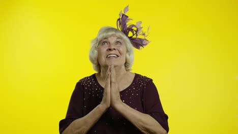 positive senior old blond woman appealing to camera, keeping prayer gesture and asking help