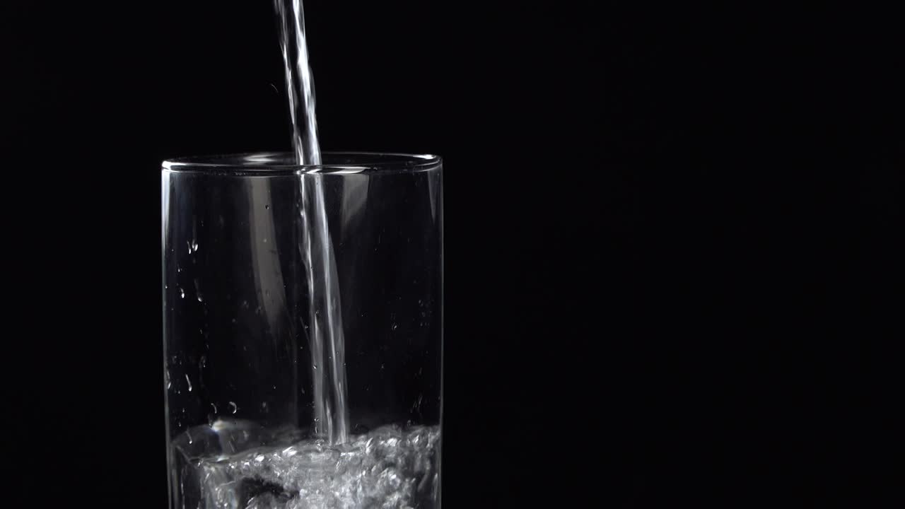 derramando água mineral fresca em um copo em uma mesa. bebida espumante fresca com bolas de oxigênio em fundo preto